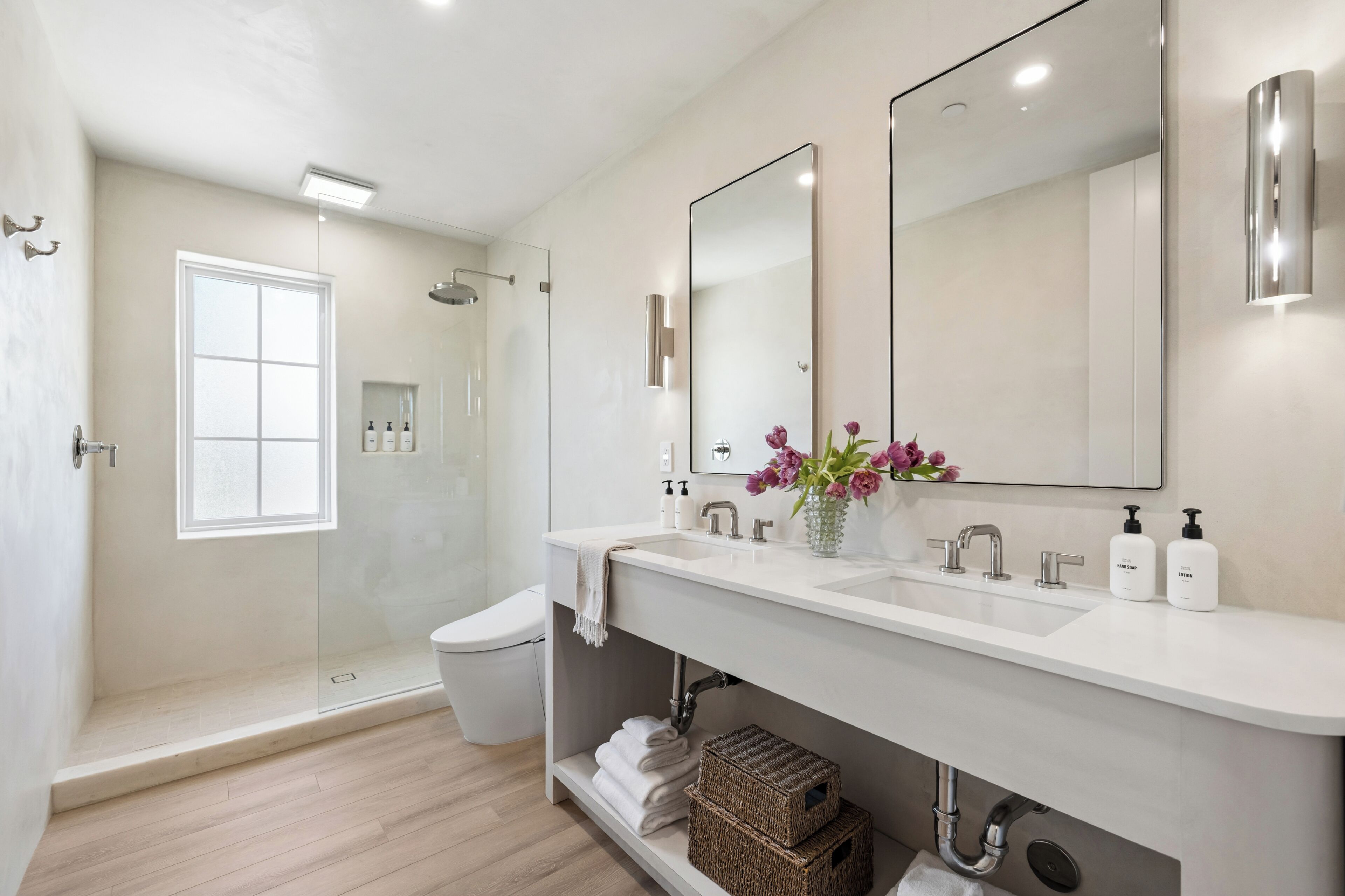 A modern bathroom with a glass-enclosed shower, a large mirror, and a white vanity.