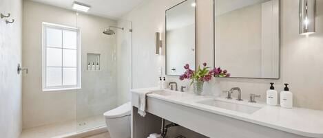 A modern bathroom with a glass-enclosed shower, a large mirror, and a white vanity.