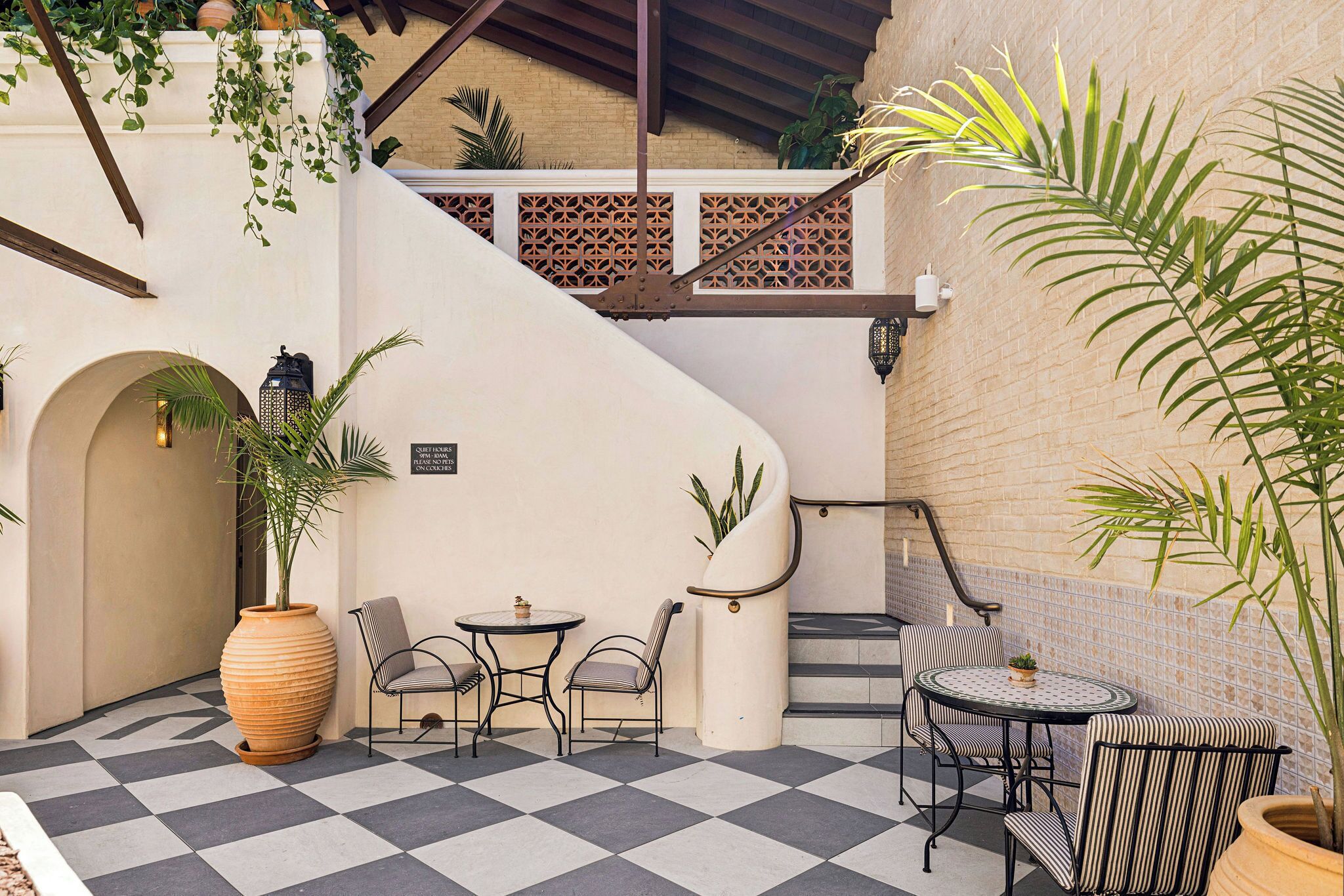 Un patio al aire libre con piso a cuadros, asientos, una escalera y plantas en macetas.