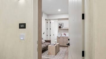 A hallway leading to a living area with a sofa, a coffee table, and a kitchen area with cabinets and a countertop.