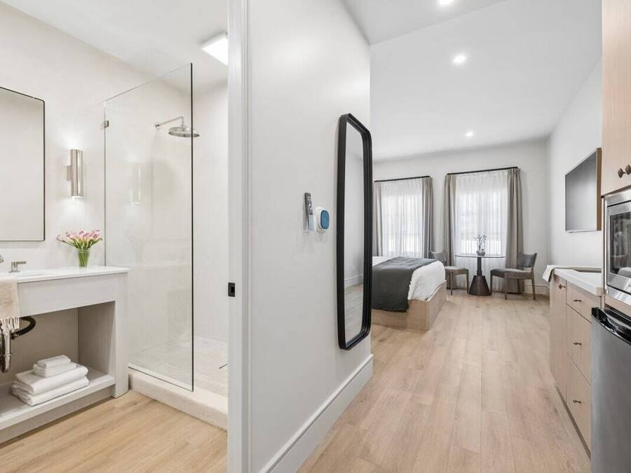 A modern hotel room with a shower, a bed, a dining area, and a kitchen.