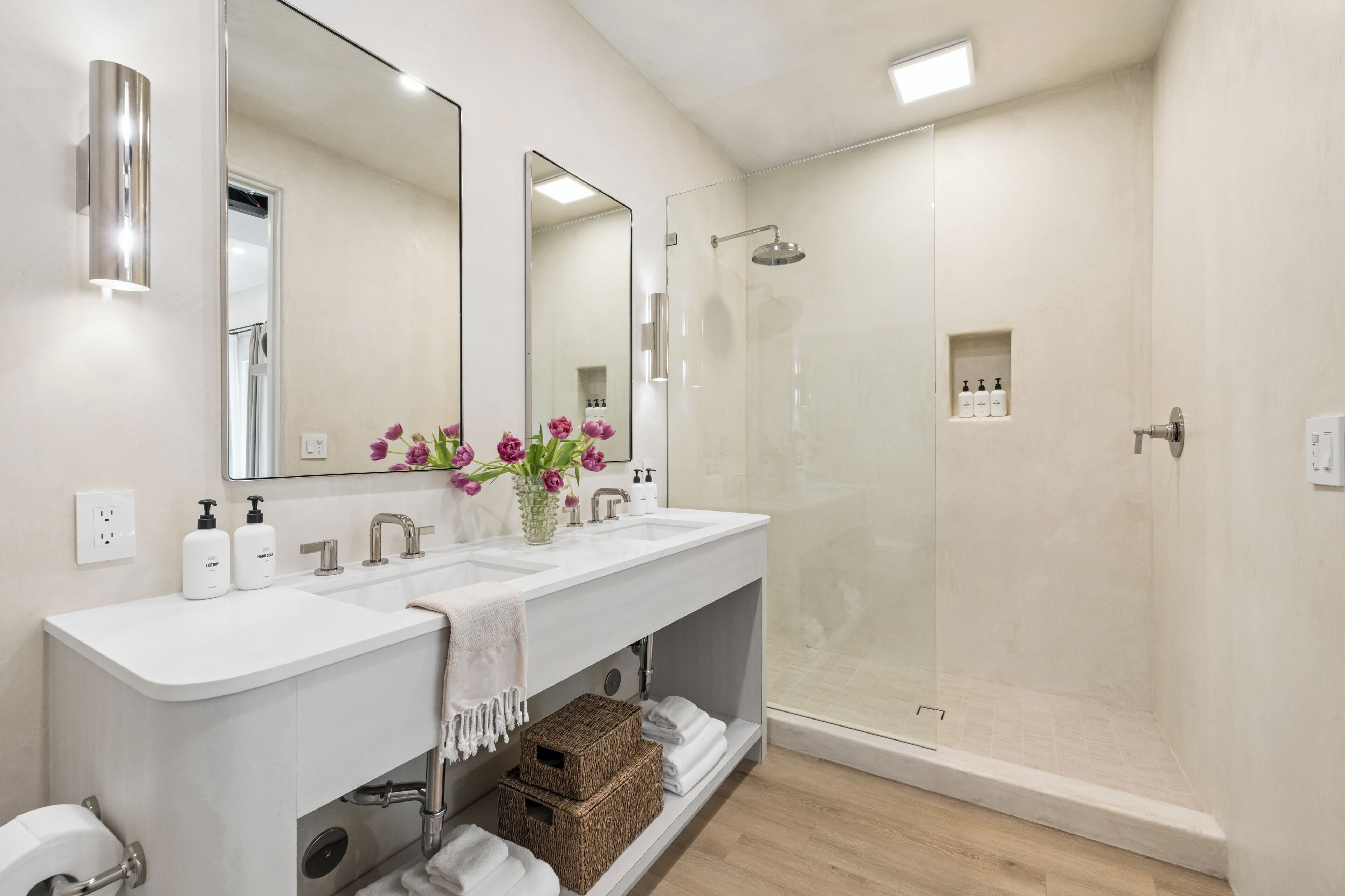 A modern bathroom with a large mirror, two sinks, a shower, and a towel rack.