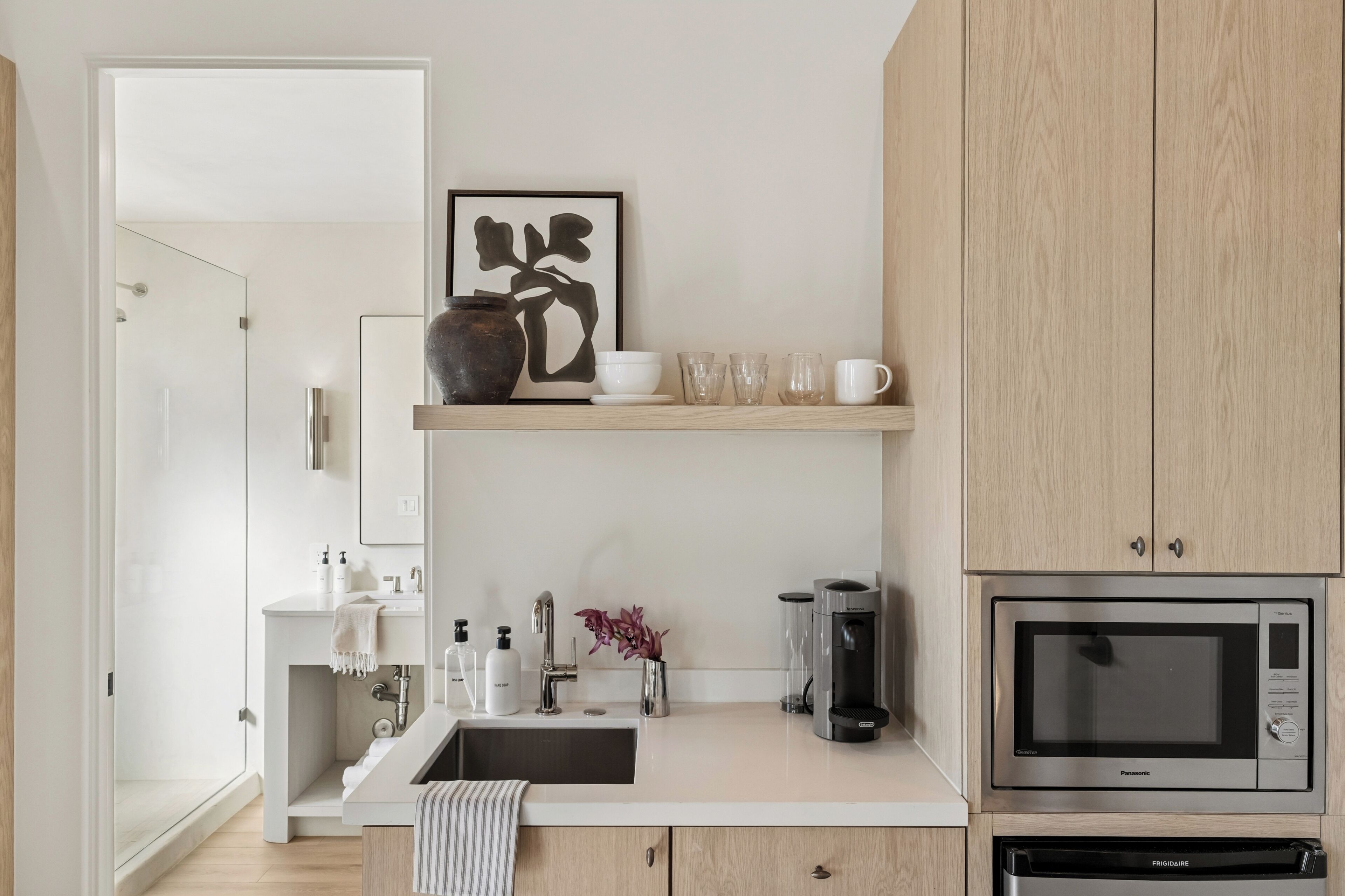 A modern kitchen with a built-in microwave, coffee maker, and a shelf with cups and a vase.