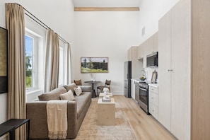 Una sala de estar moderna con sofá, mesa de centro y área de cocina con armarios y electrodomésticos.