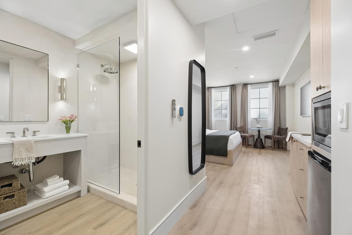 Moderni hotellihuone, jossa on suihku, sänky, ruokailutila ja keittiö.
