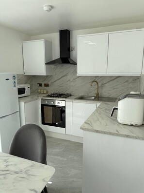 A modern kitchen with white cabinets, a gas stove, a microwave, and a sink. - “Large Newcastle Home for 8– 4 guest Bedrooms, 5 Beds (Newcastle upon Tyne)
