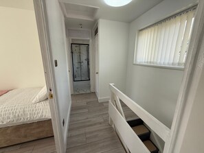 A bedroom with a bed, a bathroom with a glass shower, and a staircase with a window. - “Large Newcastle Home for 8– 4 guest Bedrooms, 5 Beds (Newcastle upon Tyne)