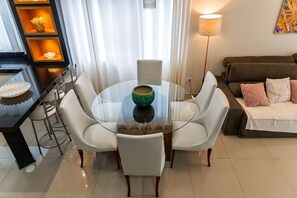 A modern living room with a glass dining table, white chairs, a sofa, and a lamp. - Casa c Churrasqueira a 300m da Praia de Massagua u (Caraguatatuba)