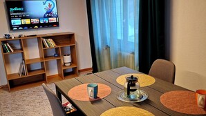 Een eetgedeelte met een houten tafel, stoelen en een aan de muur bevestigde televisie.
