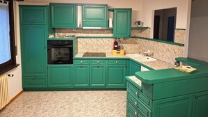 Een keuken met groene kastjes, een inbouwoven, een spoelbak en een aanrecht met een waterkoker.
