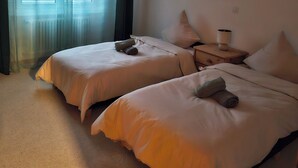 Een hotelkamer met twee bedden, een nachtkastje, een lamp, een schilderij en een raam met gordijnen.