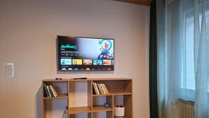 Een woonkamer met een aan de muur bevestigde televisie, een houten boekenkast en een raam met gordijnen.