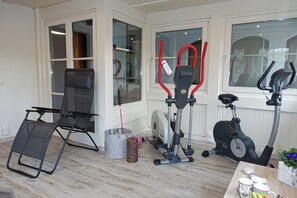 Ein Heimfitnessraum mit Trainingsgeräten, einem Klappstuhl und einem Couchtisch mit Tassen.