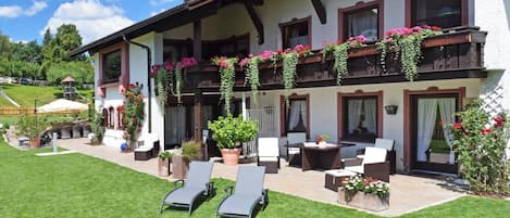 A two-story building with a balcony adorned with flowers, outdoor seating, and a well-maintained lawn.