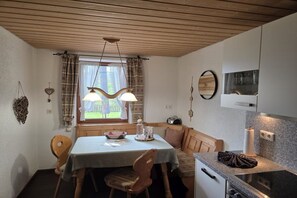 Eine gemütliche Küche mit Holzboden, einem Esstisch mit Stühlen, einem Fenster mit Vorhängen und einer Mikrowelle über der Arbeitsfläche.