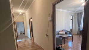 A hallway with wooden flooring, a door leading to a living area with a sofa, a table, and a chair. - Wonderful 2-bedroom apartment with AC in vibrant Yerevan 🫶✨💖 (Yerevan)