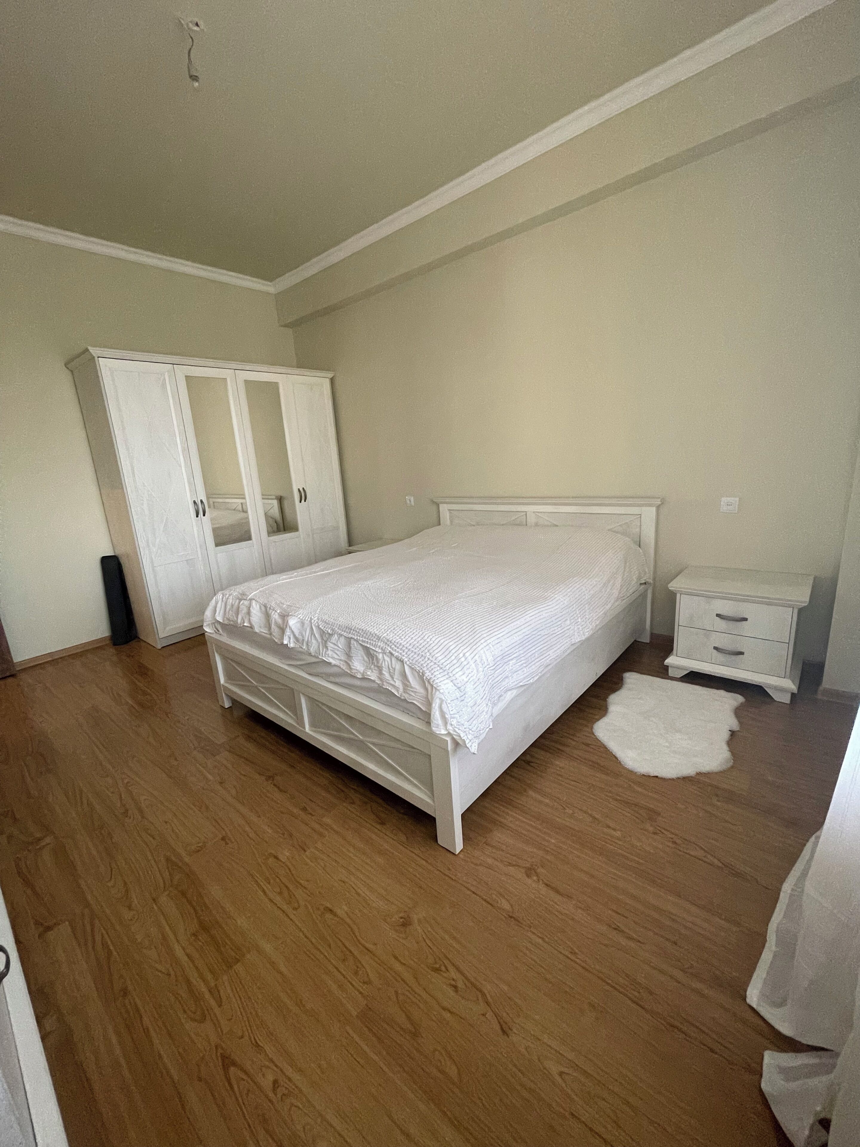 A bedroom with a bed, a wardrobe, a nightstand, and a white rug.