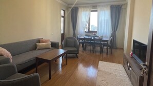 A living room with a sofa, armchairs, a coffee table, a TV on a wooden cabinet, and a dining area with a table and chairs. - Wonderful 2-bedroom apartment with AC in vibrant Yerevan 🫶✨💖 (Yerevan)