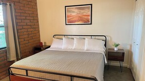 A bed with a metal frame, a bedside table with a plant, and a framed picture on the wall.