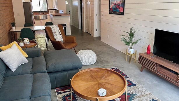 A modern living room with a sofa, a coffee table, a TV, and a kitchen in the background.