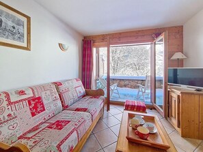 A living room with a sofa, a wooden cabinet, a television, and a table with cups. - 100m from ski slopes, Ground floor, swimming pool, terrace, tv, ski locker, 32m², Les Menuires (Les Menuires)