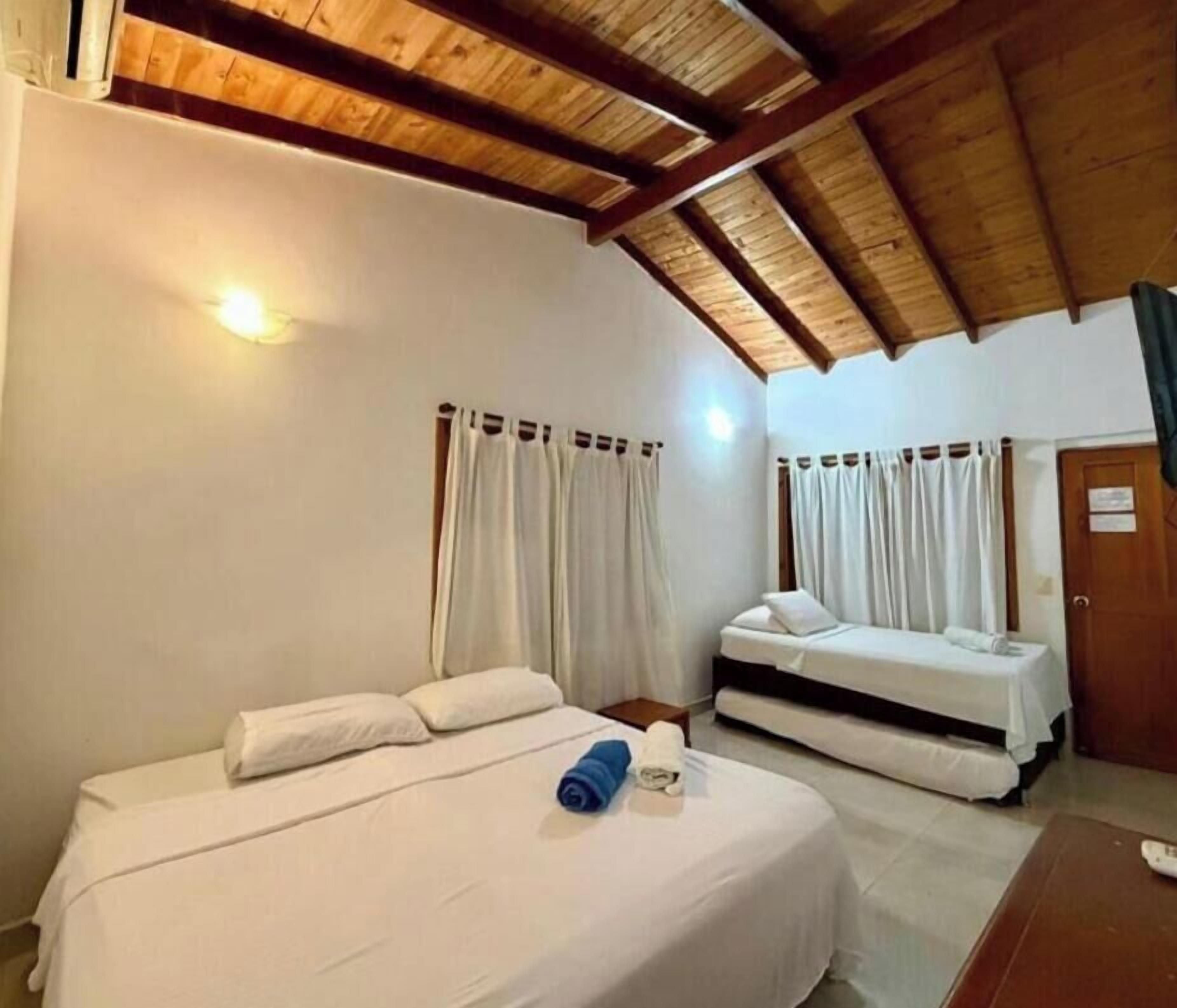 Una habitación con dos camas, vigas de madera en el techo, cortinas blancas y una puerta de madera.