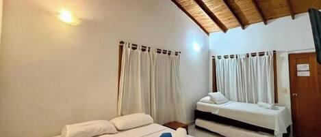 Una habitación con dos camas, vigas de madera en el techo, cortinas blancas y una puerta de madera.