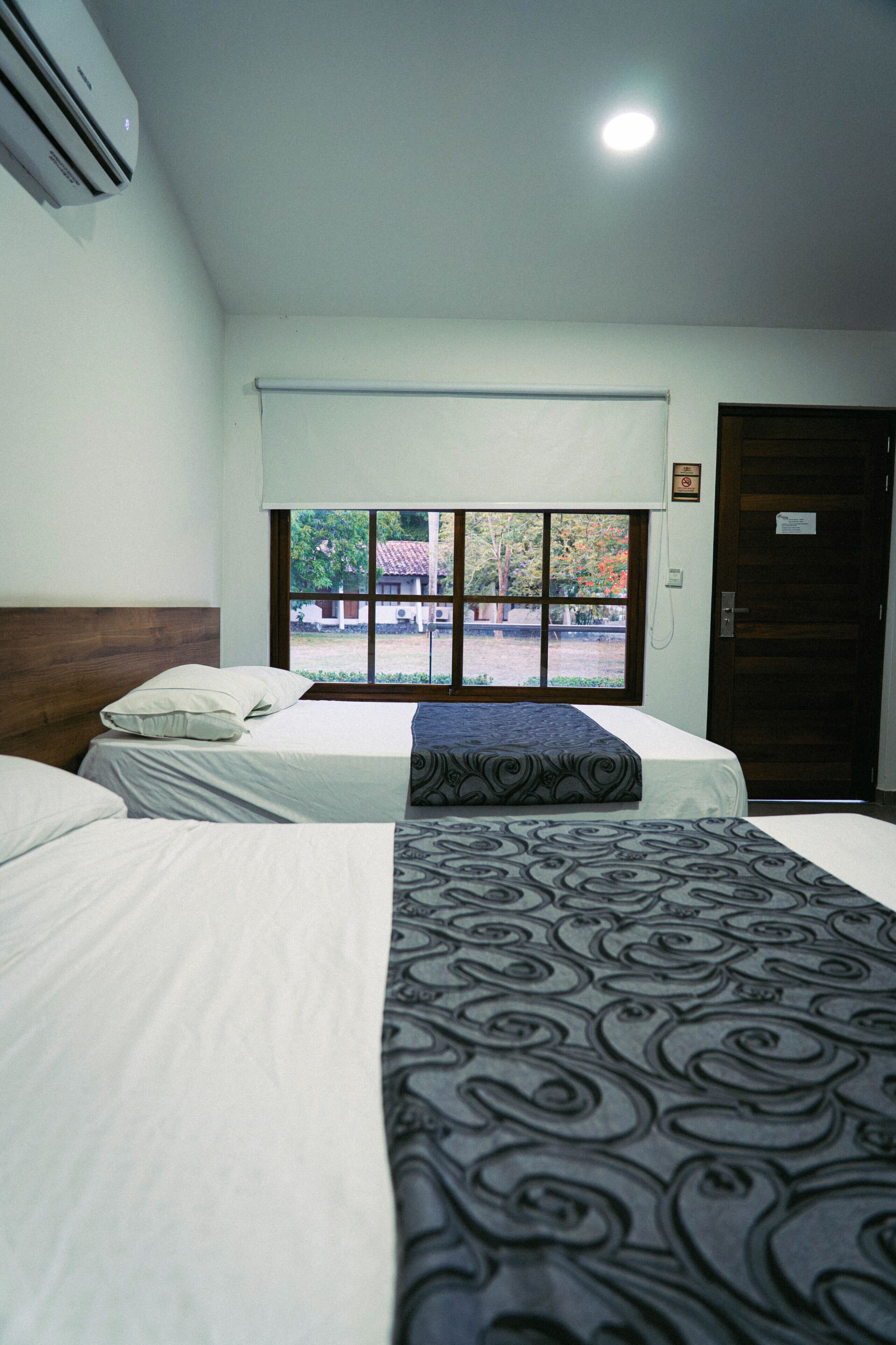 Une chambre d’hôtel avec deux lits, une fenêtre donnant sur l’extérieur et une porte avec une pancarte.