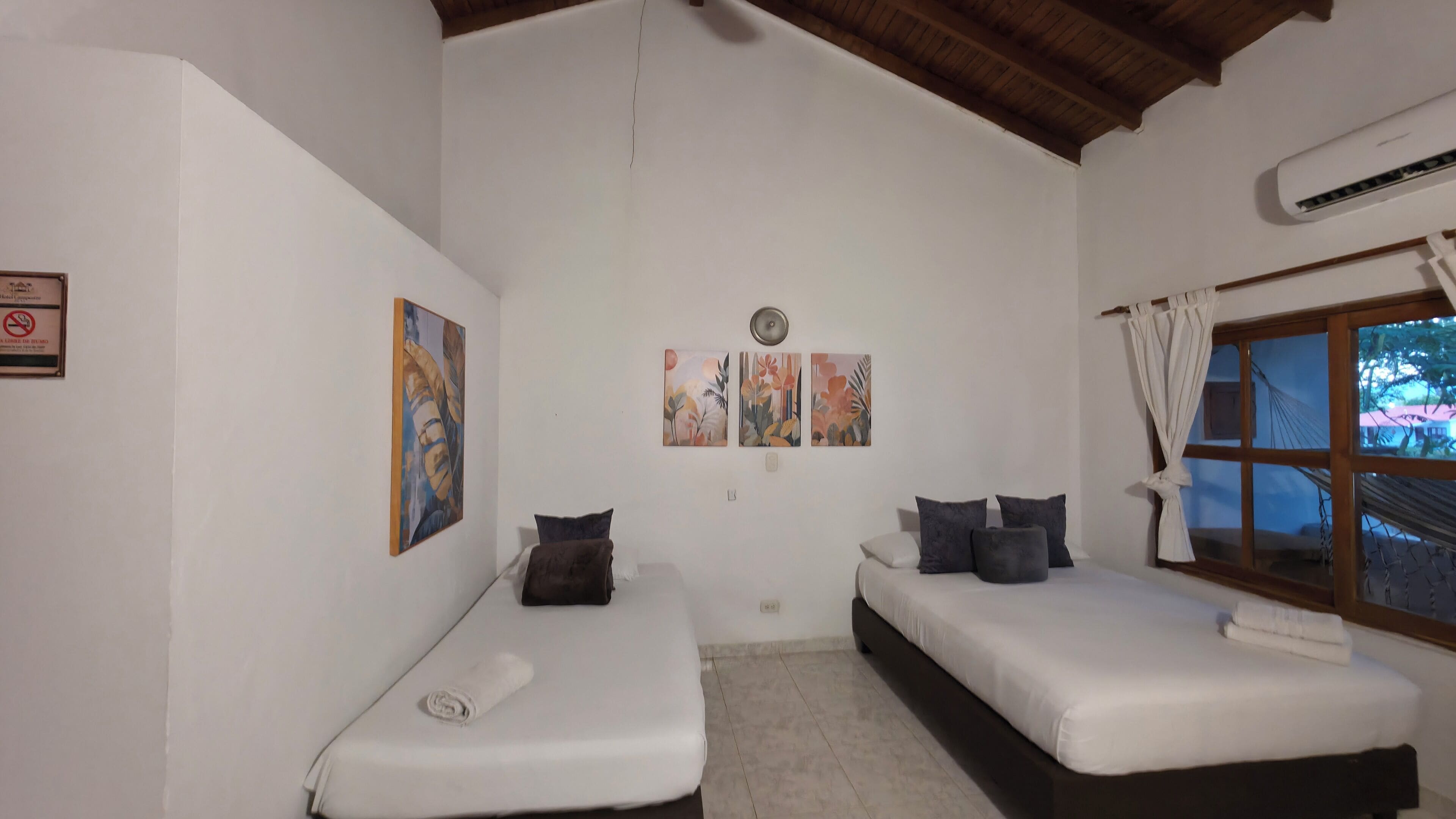 Una habitación con dos camas individuales, una ventana con cortinas y cuadros colgados en la pared.