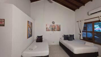 Una habitación con dos camas individuales, una ventana con cortinas y cuadros colgados en la pared.
