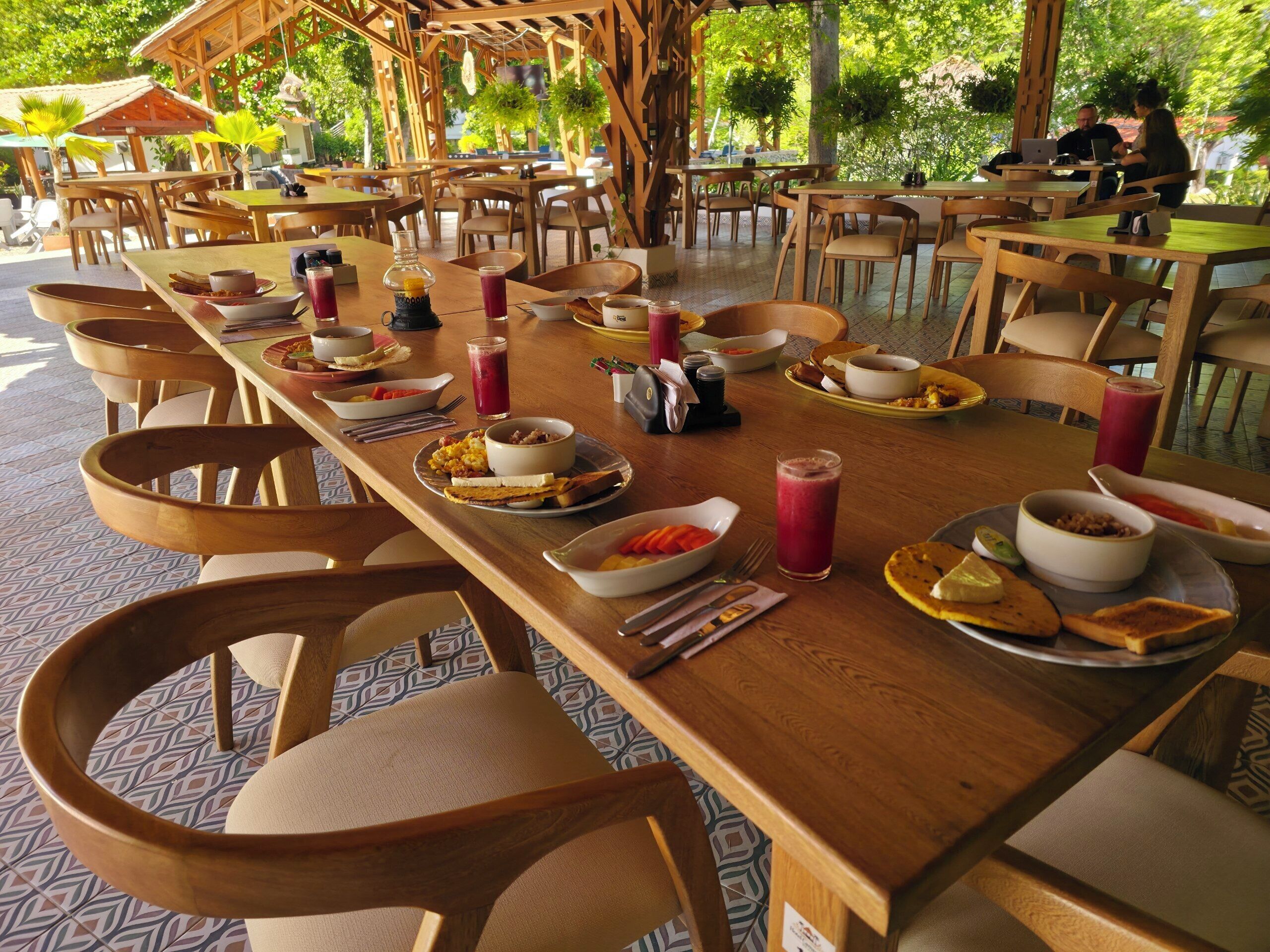 A restaurant with wooden tables and chairs, outdoor seating, and a variety of dishes and drinks.