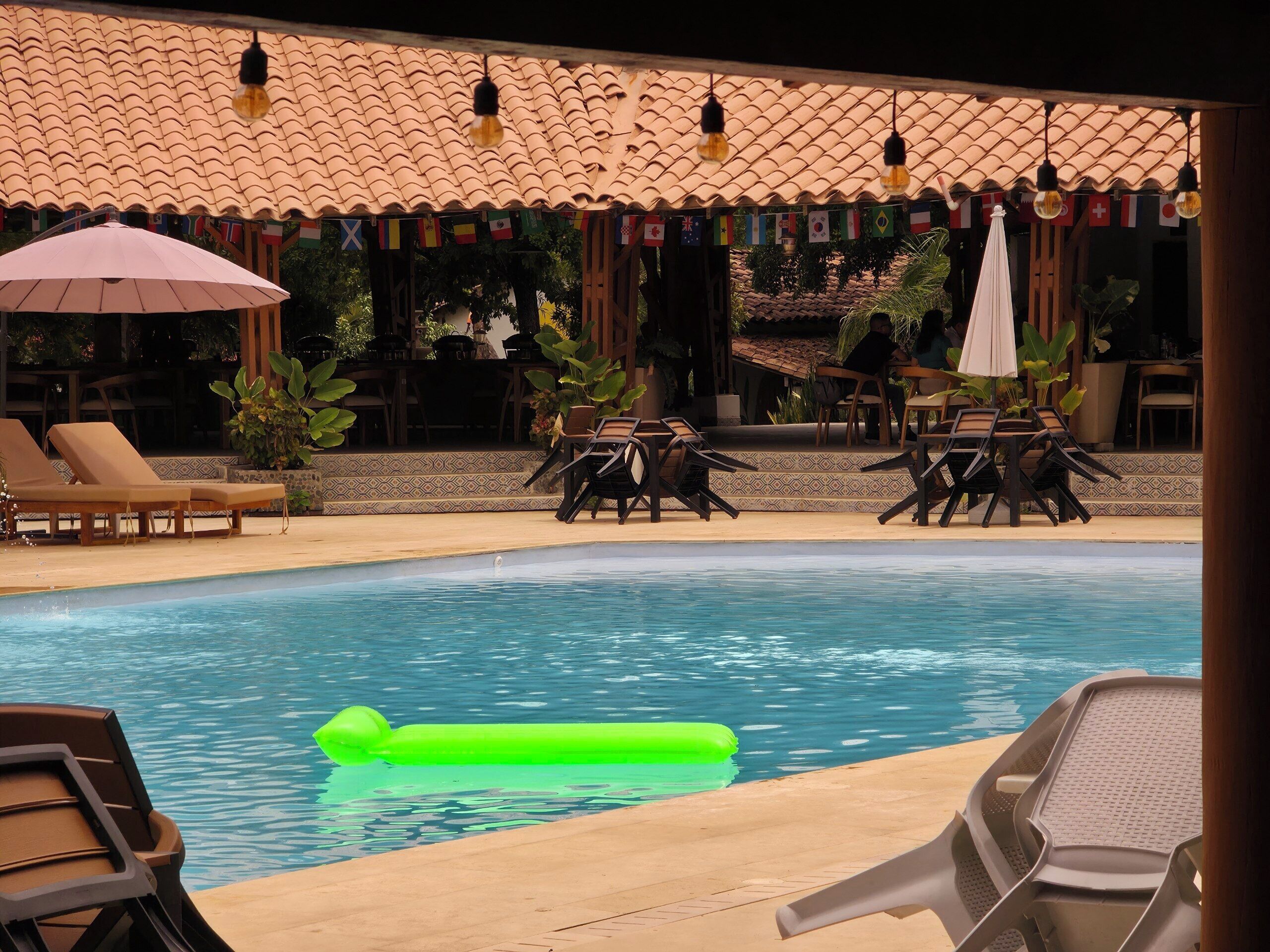 A pool area with lounge chairs and umbrellas, surrounded by a tiled roof and potted plants.