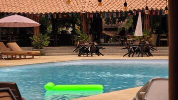 A pool area with lounge chairs and umbrellas, surrounded by a tiled roof and potted plants.