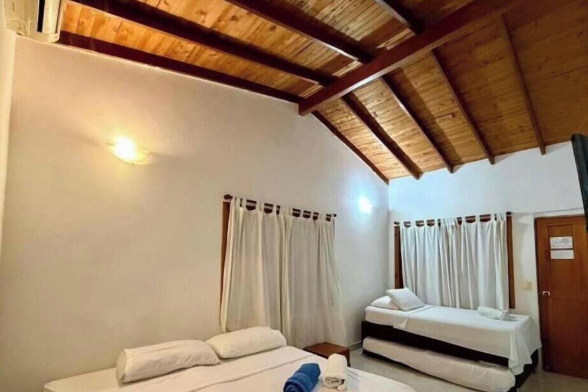 A room with two beds, wooden ceiling beams, white walls, and curtains.