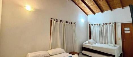 A room with two beds, wooden ceiling beams, white walls, and curtains.