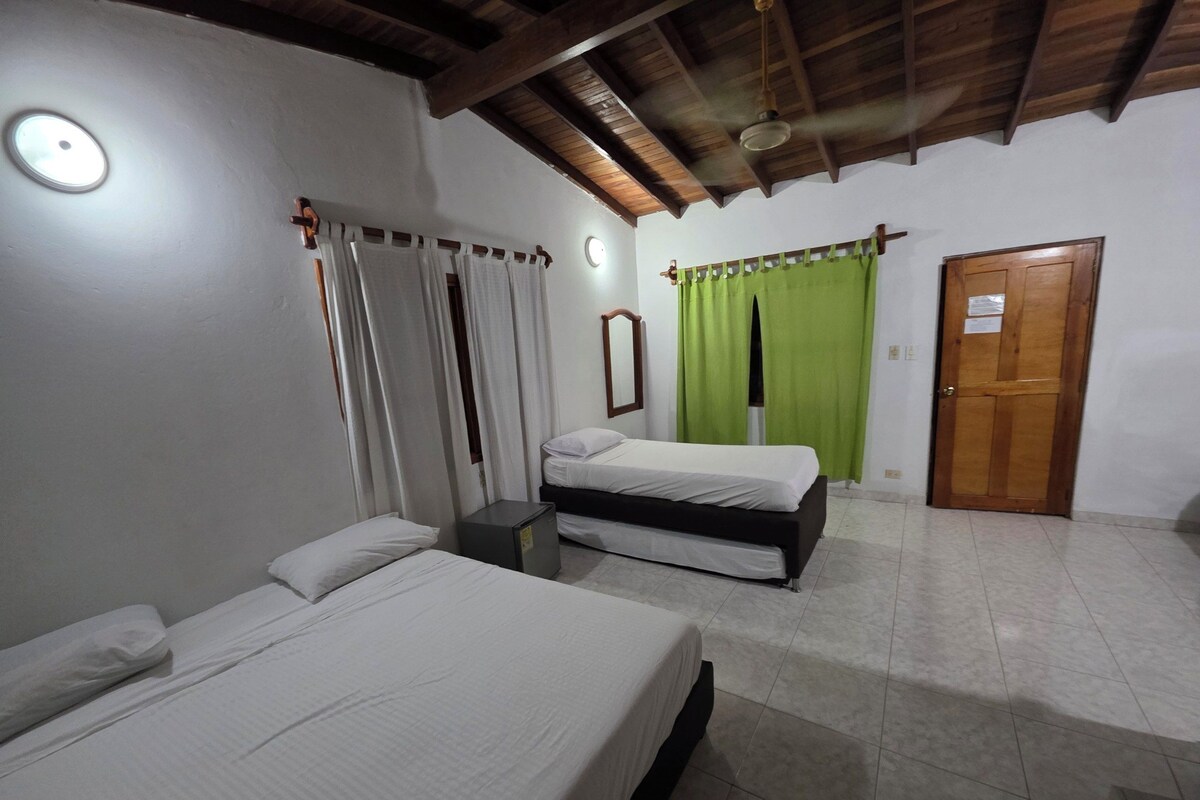 A room with two beds, a small table, a mirror, a door, and a ceiling fan.