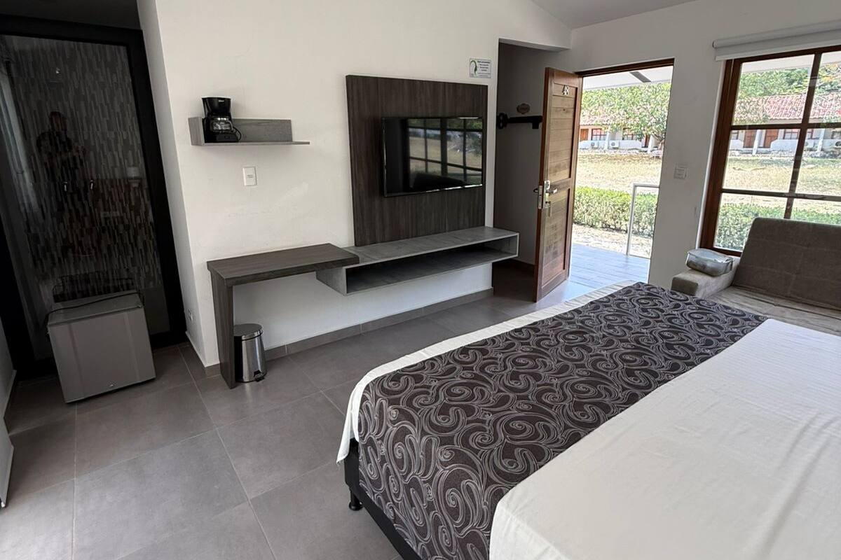 A modern bedroom with a bed, a TV mounted on a wall, a small shelf, and a door leading to a balcony.