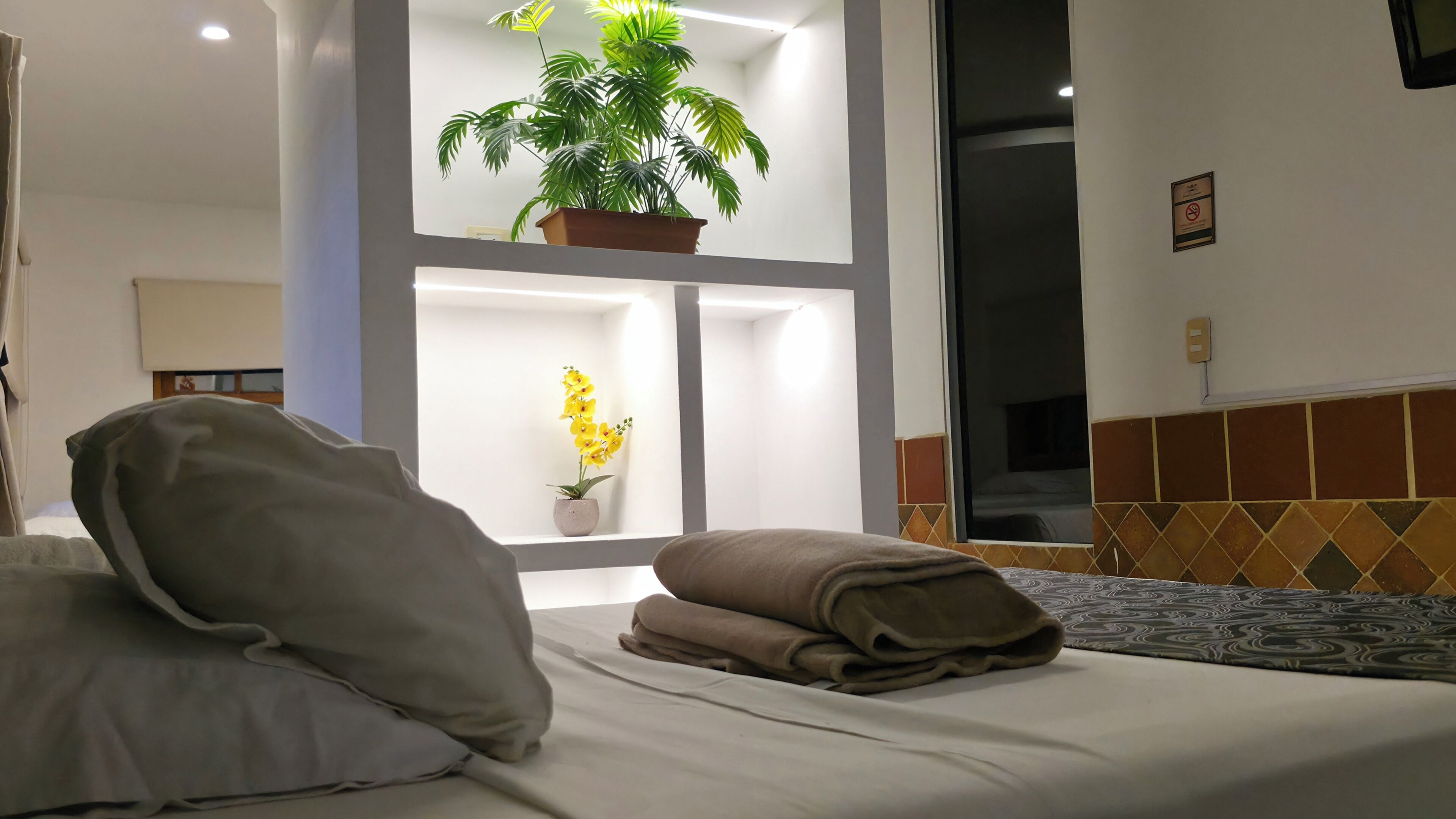 A hotel room with a bed, pillows, a potted plant, and a window.