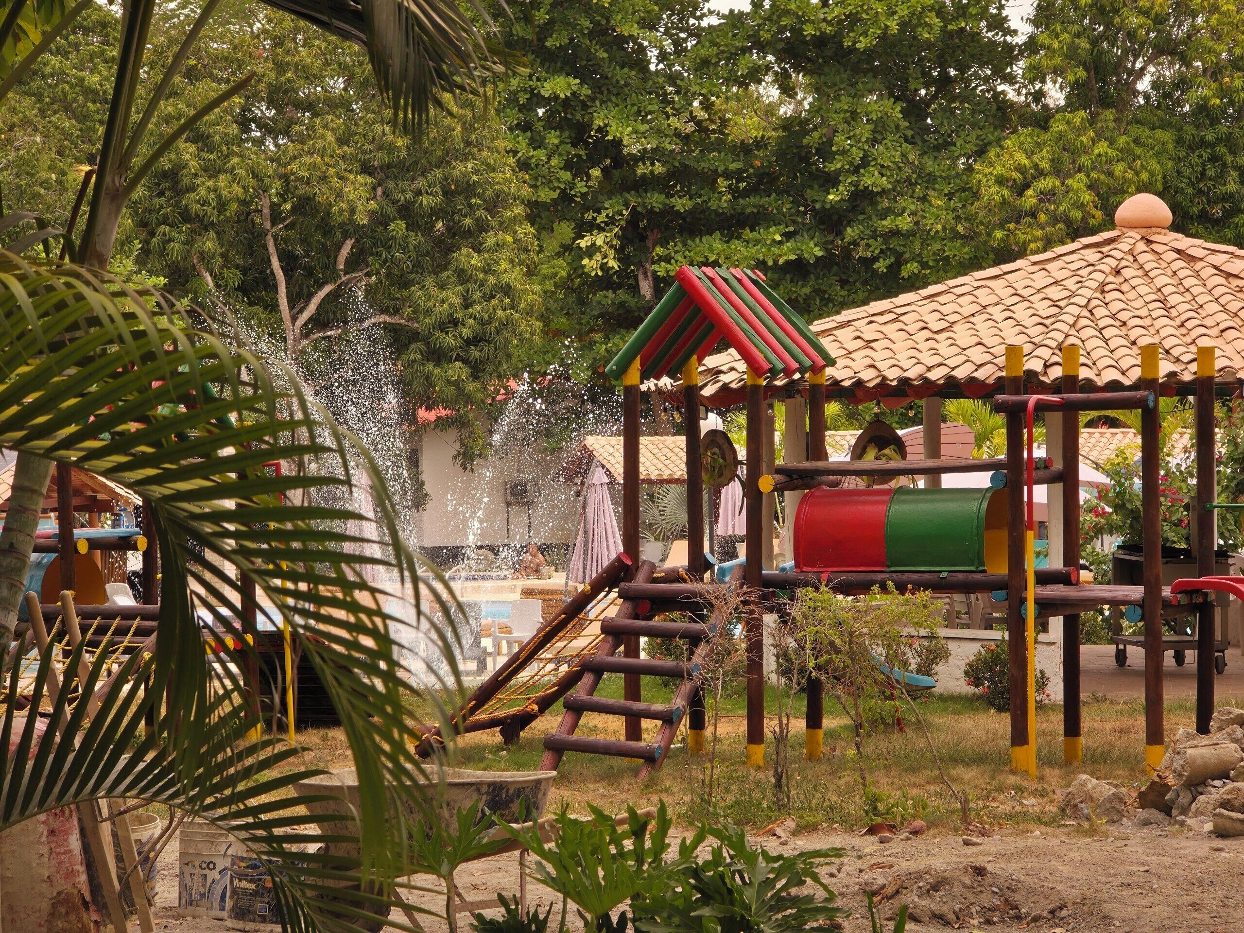 Un parque infantil con tobogán, estructuras para escalar y fuente de agua.