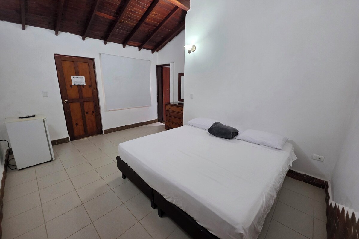 A bedroom with a bed, a dresser, a small refrigerator, and a door with a sign.