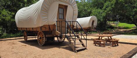 A covered wagon with a wooden structure, a wooden bench, and a gravel area.