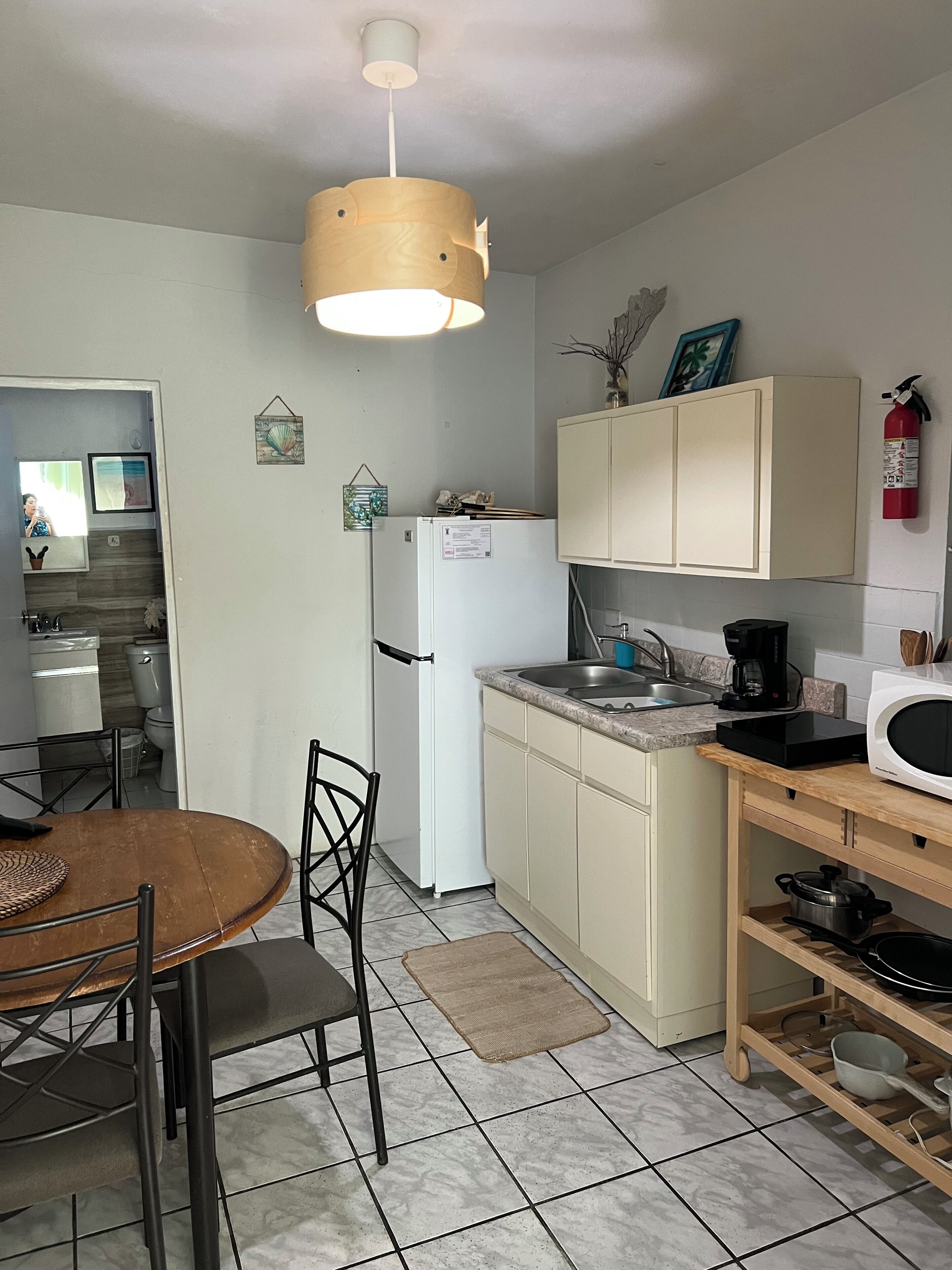 A compact kitchen with a refrigerator, microwave, sink, and a dining area with chairs and a table.