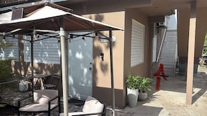 A covered patio area with a table and chairs, a potted plant, and a door.