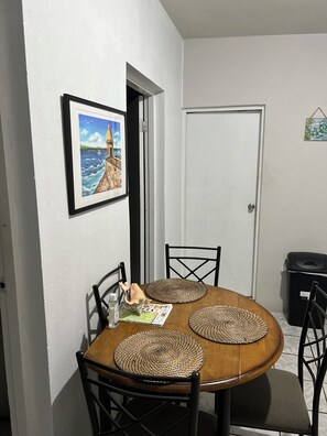 Un coin repas avec une table ronde, quatre chaises, un tableau encadré au mur et une porte.