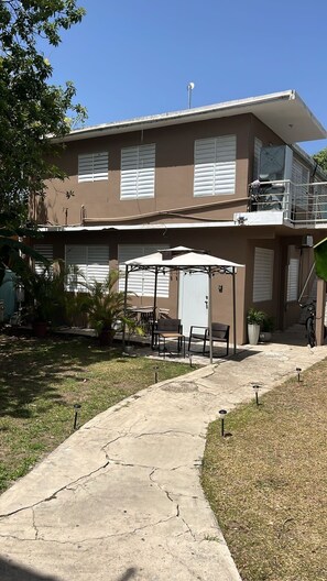 A two-story building with a covered patio area, outdoor seating, and a pathway leading to the entrance.