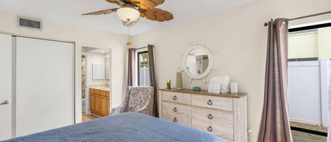 A bedroom with a bed, dresser, mirror, ceiling fan, and a view of the outdoors.