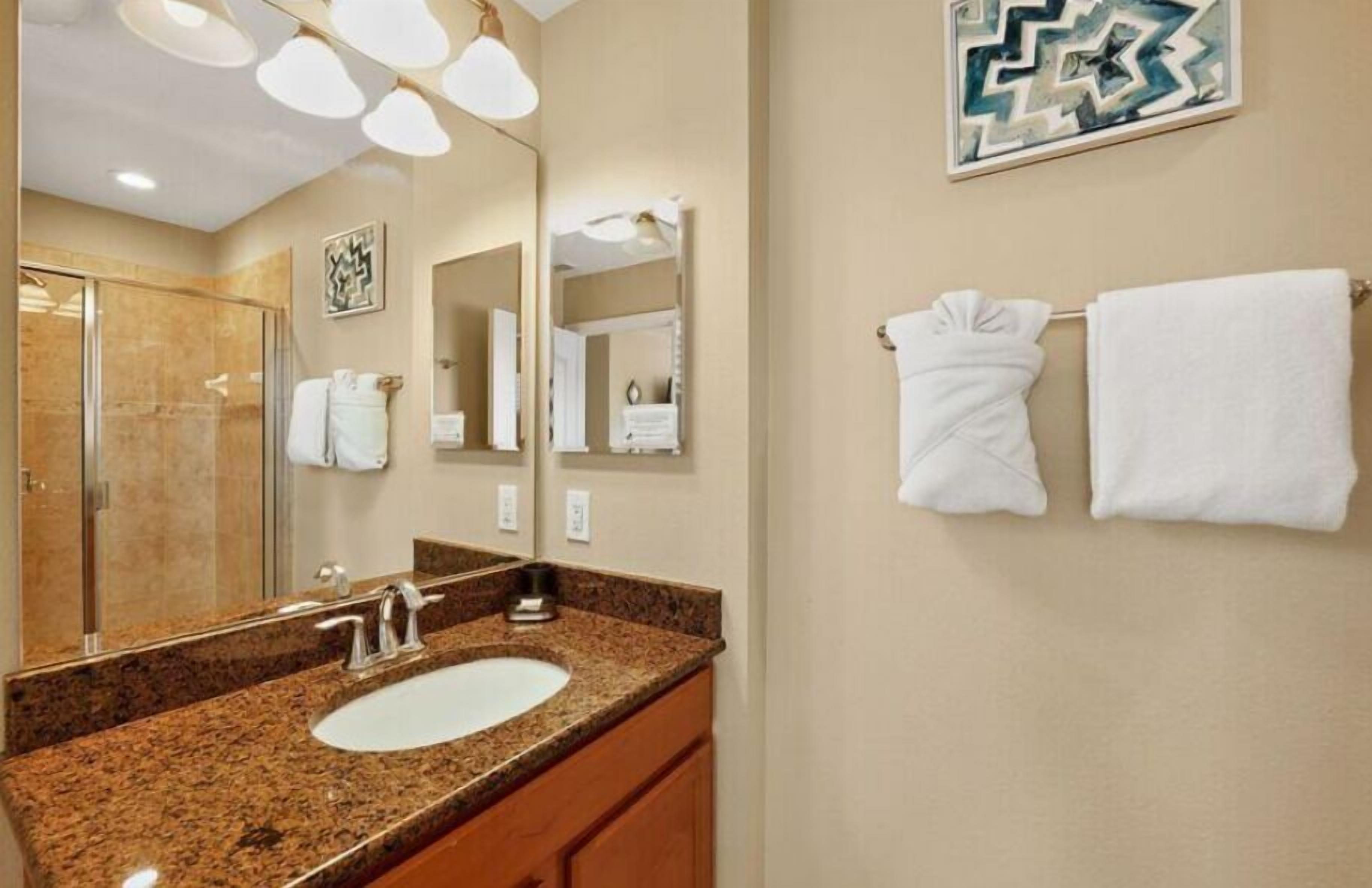 A hotel bathroom with a granite countertop sink, a large mirror, and two towels on the wall.
