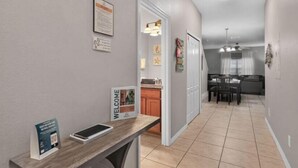 Ein Flur, der in einen Essbereich mit Tisch und Stühlen führt, mit einer Küche im Hintergrund und einem Willkommensschild an der Wand.