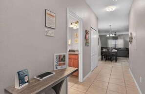 Ein Flur, der in einen Essbereich mit Tisch und Stühlen führt, mit einer Küche im Hintergrund und einem Willkommensschild an der Wand.