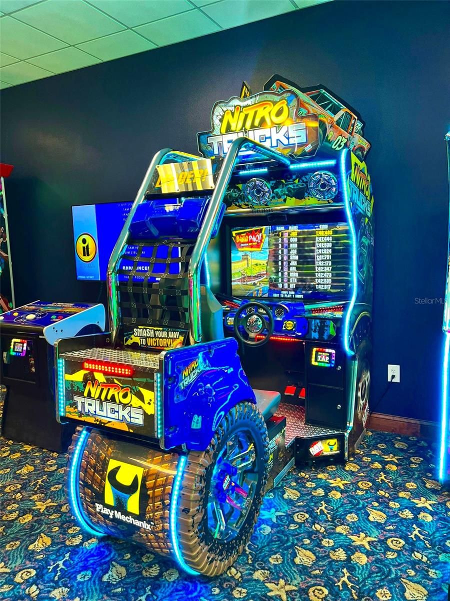A neon-lit arcade game machine with a steering wheel and dashboard, surrounded by patterned carpet.